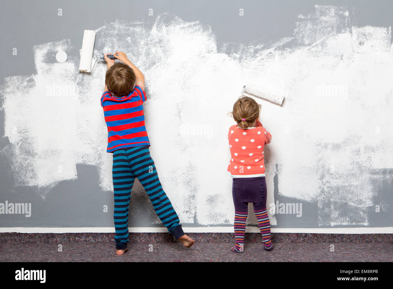 Rear view of female toddler and brother painting wall Stock Photo