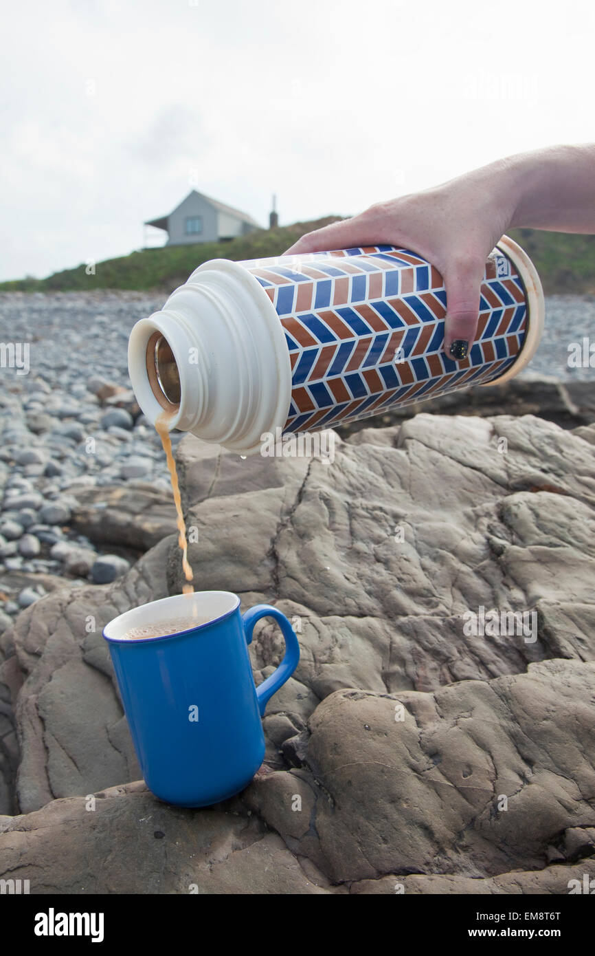 Female hand pouring tea from drinks flask on Millook Beach, Cornwall, UK Stock Photo