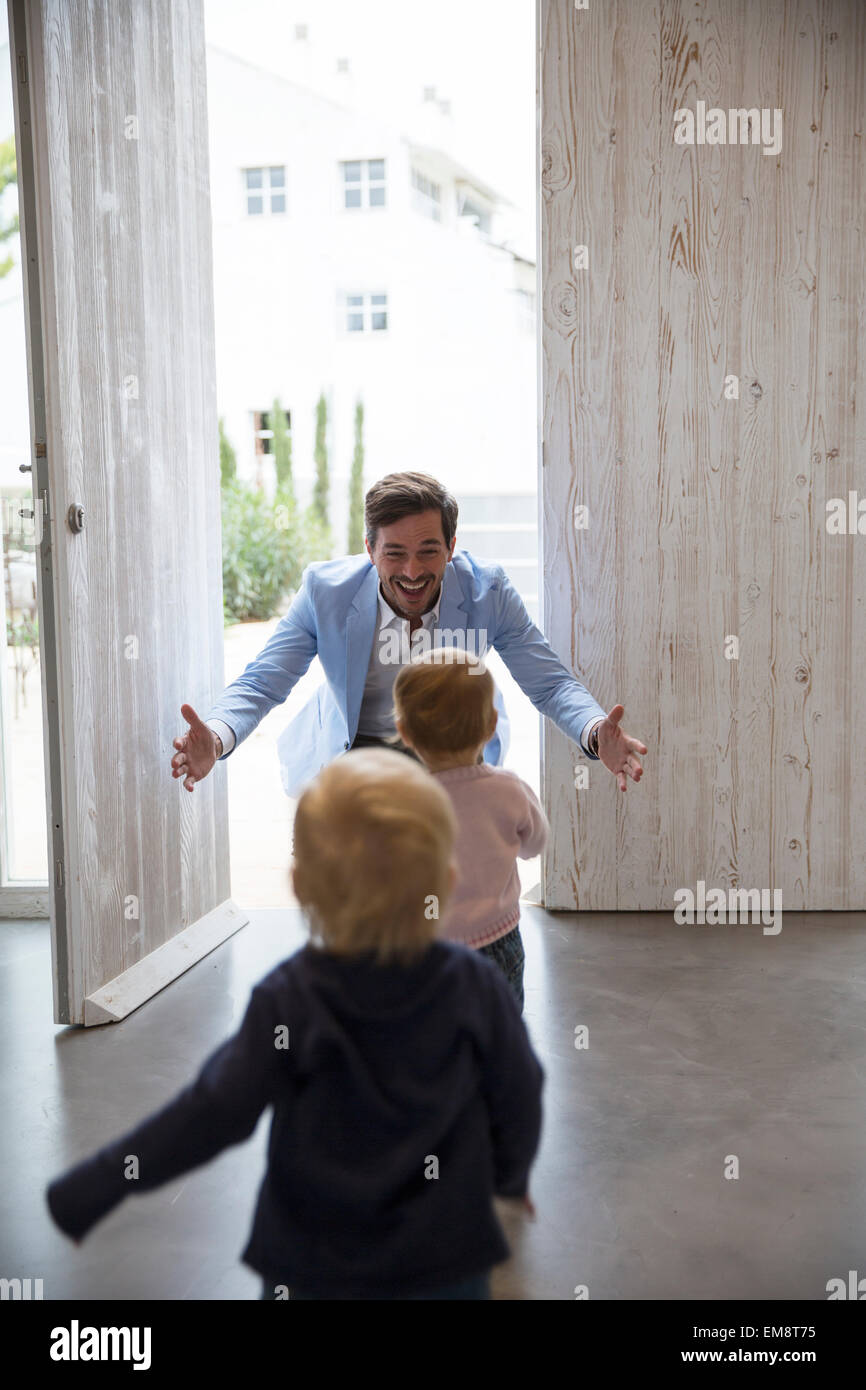 Male and female toddler twins running to fathers arms at front door Stock Photo