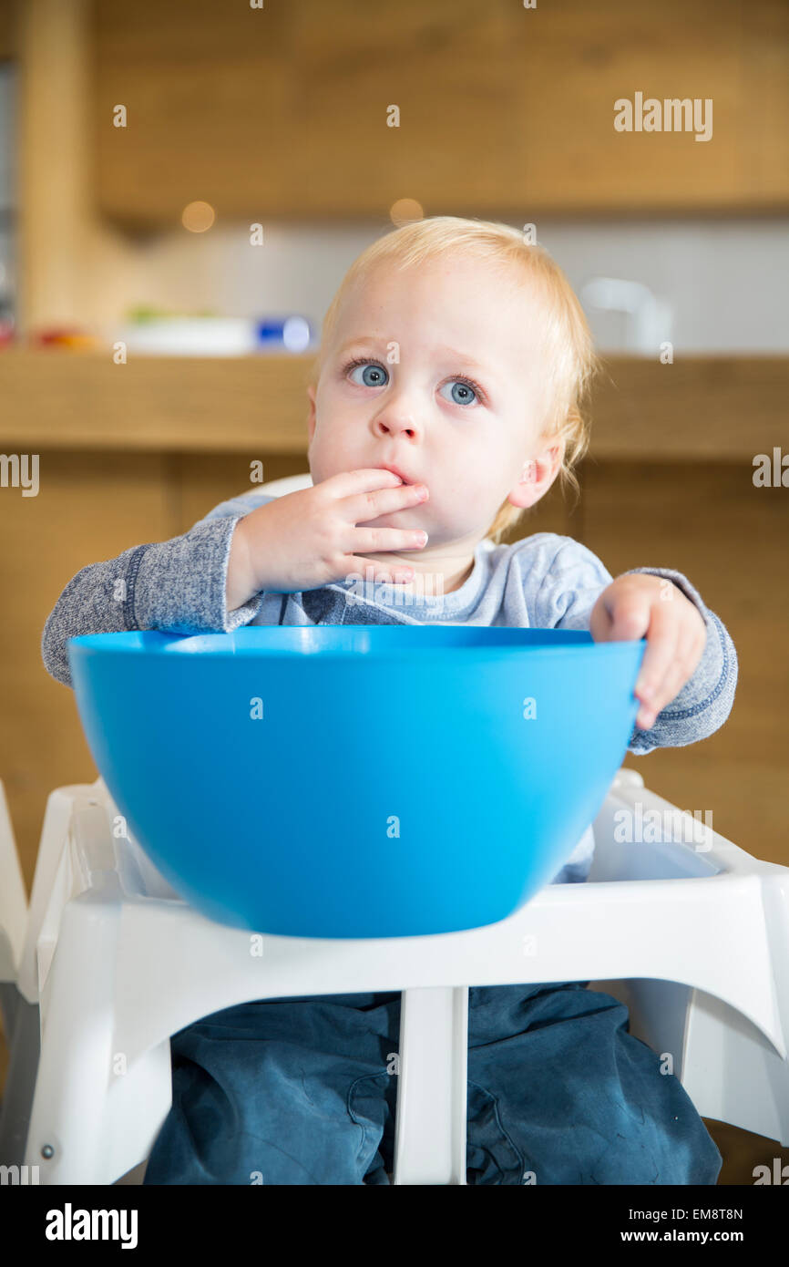 Male toddler snacking from large bowl on high chair Stock Photo