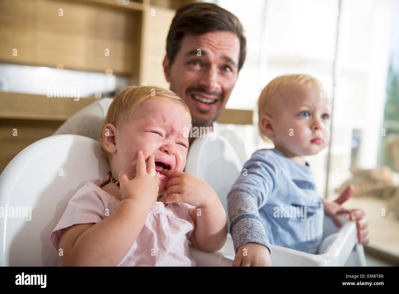 Father between male and female twin toddlers in high chairs Stock Photo