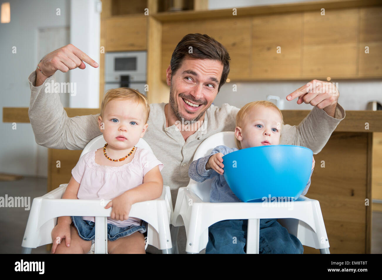Father pointing at male and female twin toddlers in high chairs Stock Photo