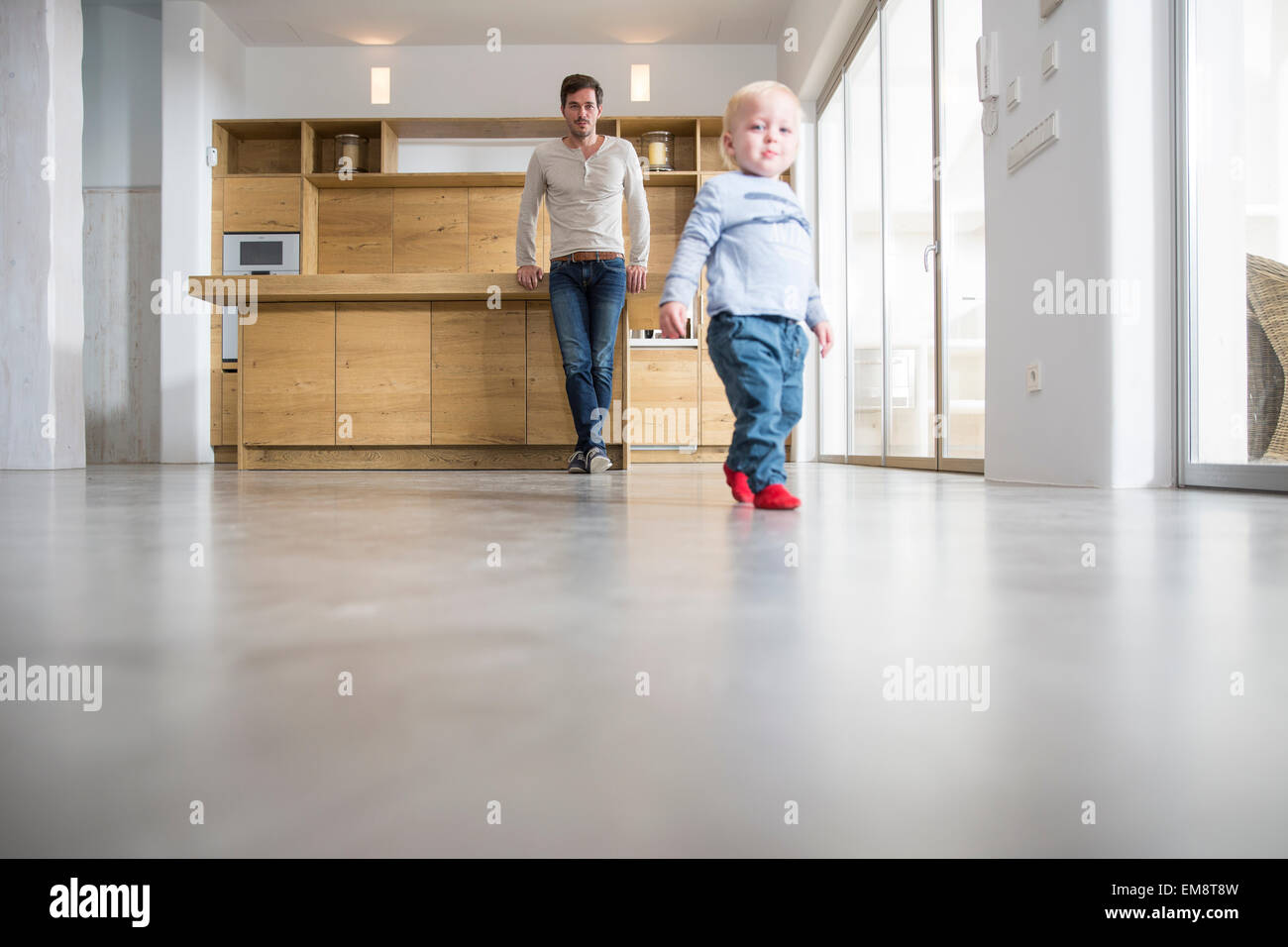 Father watching male toddlers walking on dining room floor Stock Photo