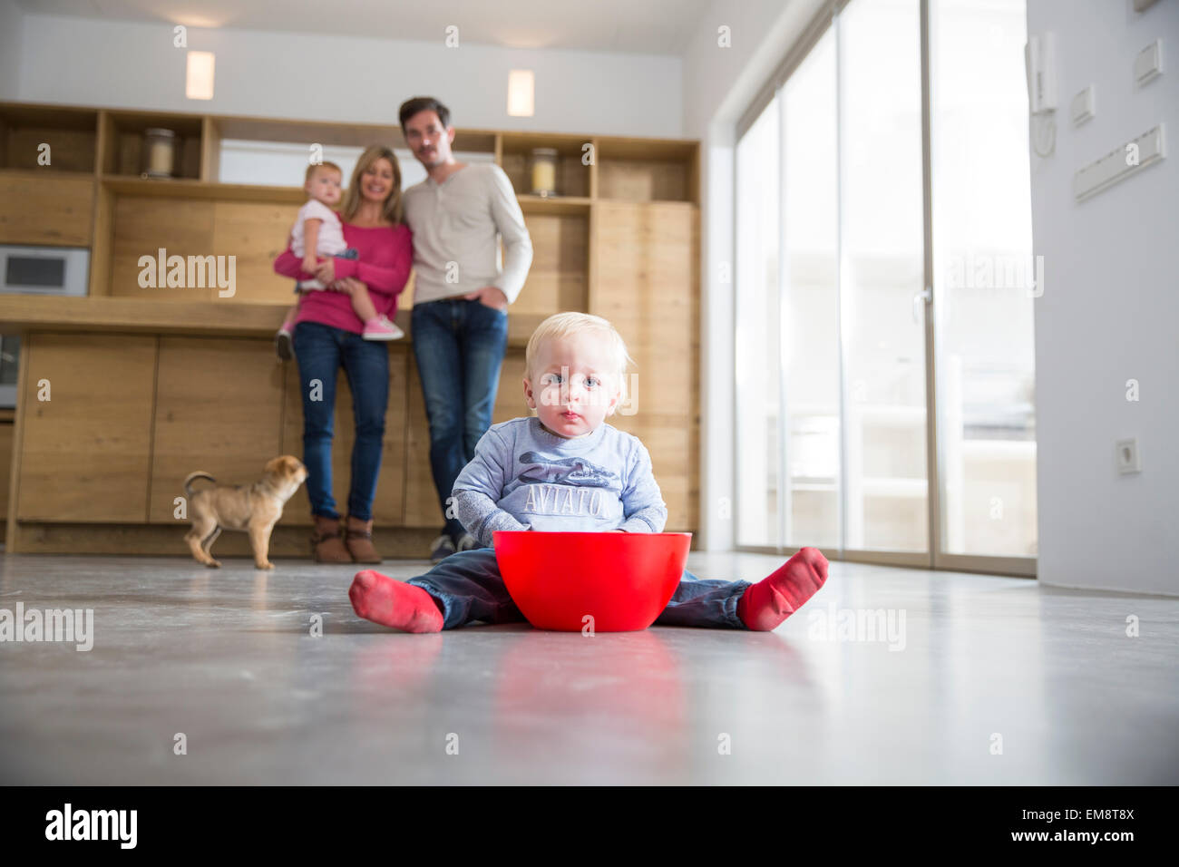 Family watching male toddler with bowl on dining room floor Stock Photo