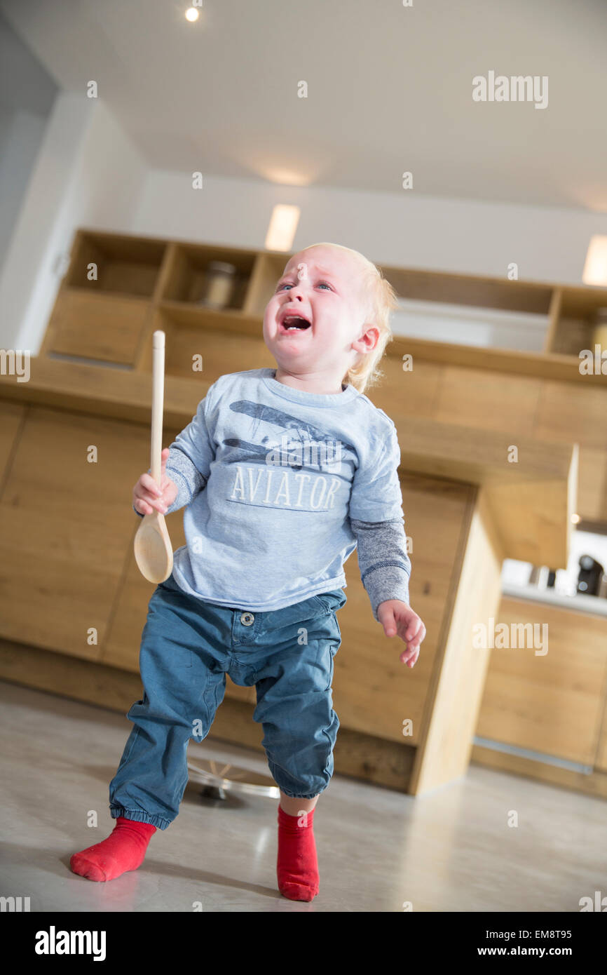 Male toddler holding wooden spoon and crying in dining room Stock Photo