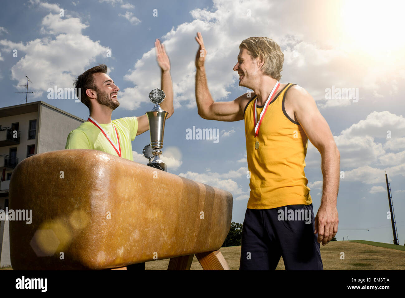 Two male gymnasts with trophy and medals giving each other high five Stock Photo