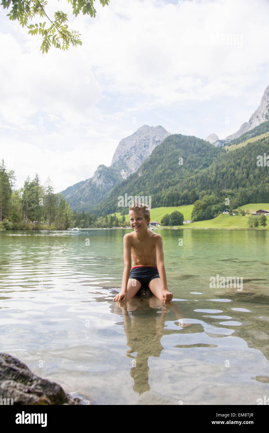 Boy sitting on rock in lake, Hintersee, Zauberwald, Bavaria, Germany Stock Photo