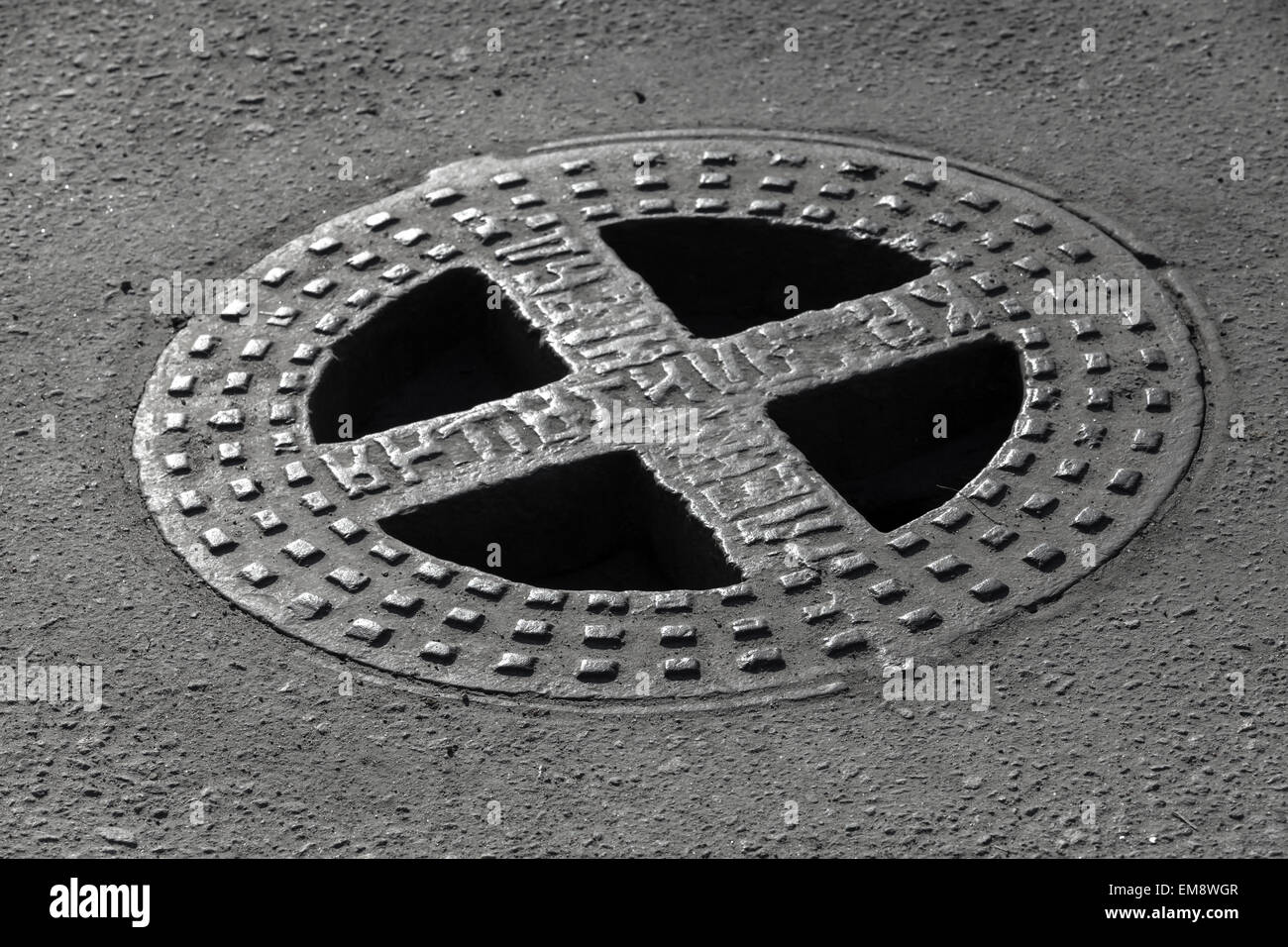 Round hatch in urban asphalt road pavement. Russian relief text on the cap means Sewerage Stock Photo