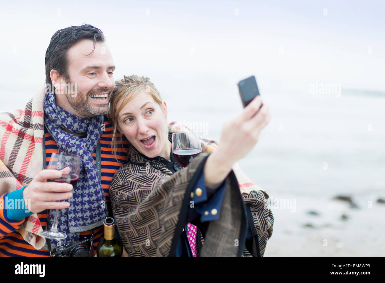 Couple on beach, drinking wine, taking self portrait using smartphone Stock Photo