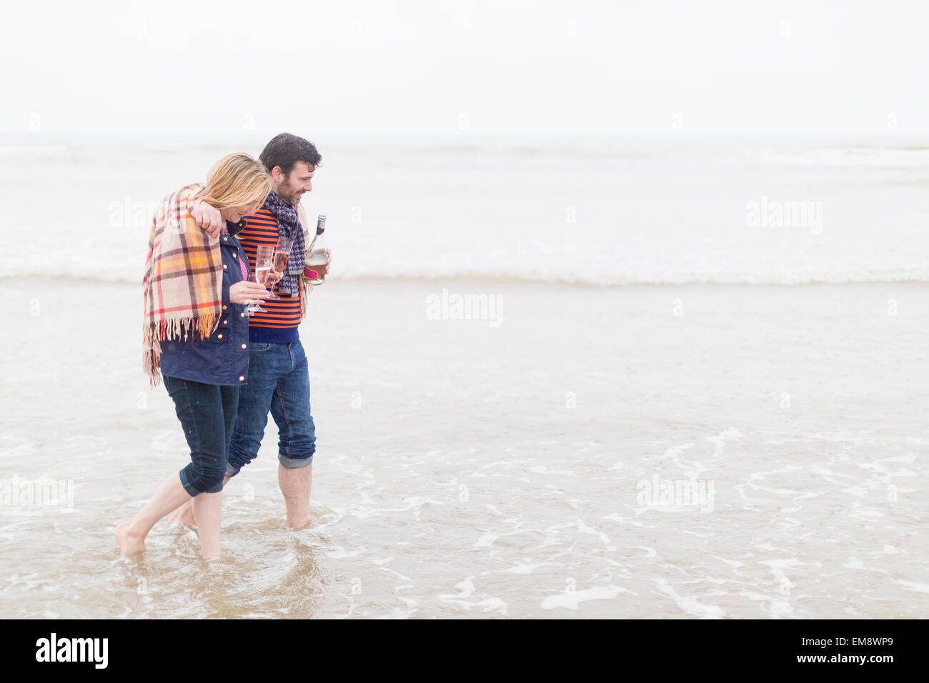 Couple walking in the sea, holding wine and wine glasses Stock Photo