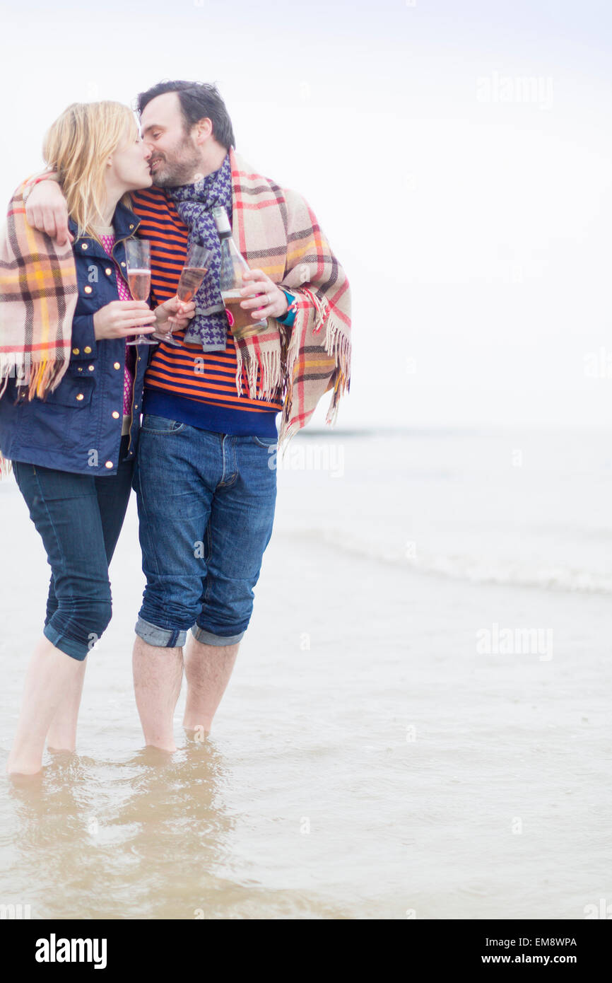 Couple walking in the sea, kissing, holding wine and wine glasses Stock Photo