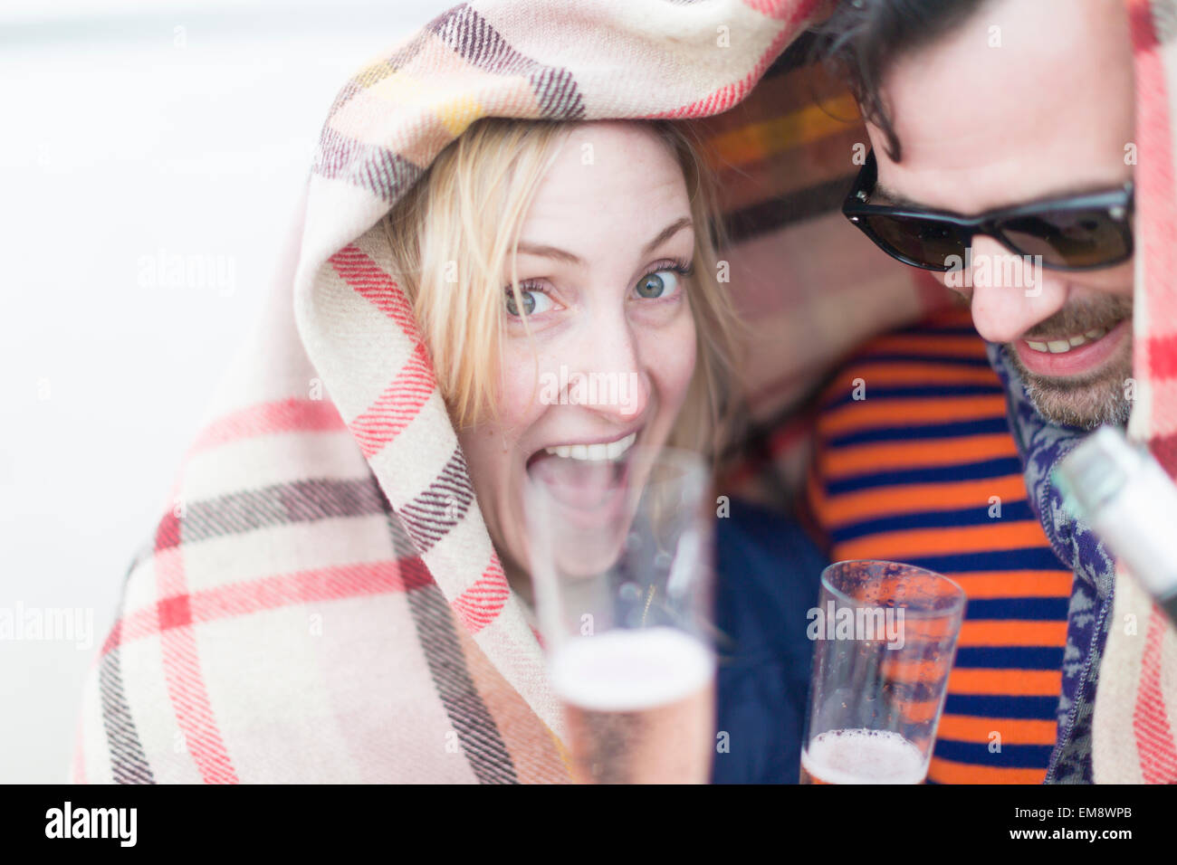 Couple drinking wine and laughing under blanket Stock Photo