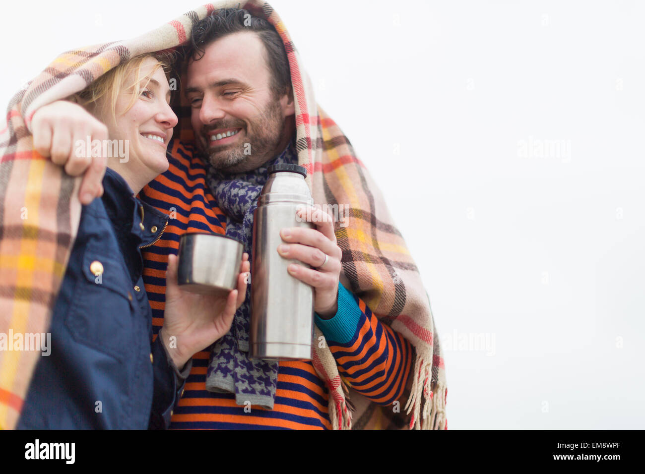 Couple outdoors, under blanket, drinking hot drink from drinks flask Stock Photo