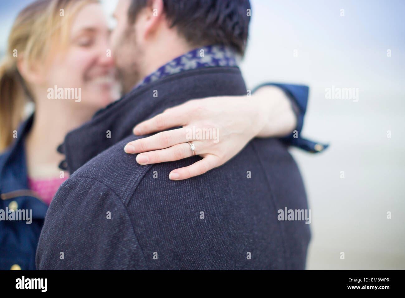 Couple on beach, embracing, woman's hand showing engagement ring Stock Photo