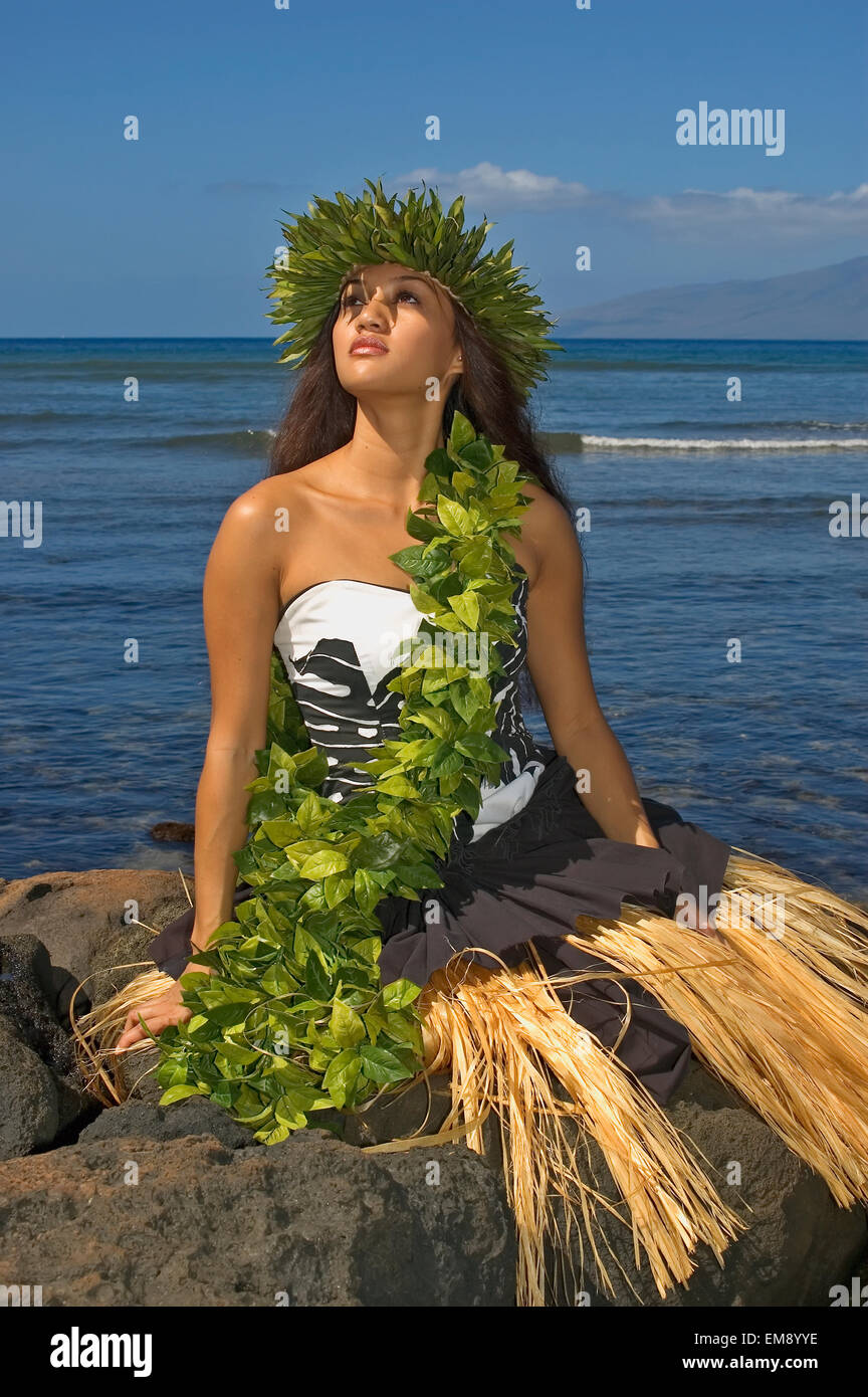 Hula Dancer With Haku Lei In Traditional Outfit On Rocky Coast, Ocean Background Stock Photo