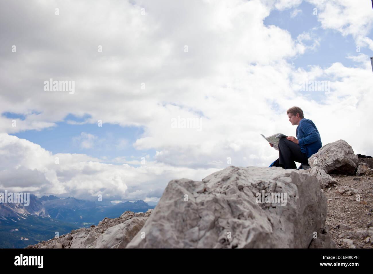 Male hiker sitting on top of mountain rock reading map, Peitlerkofel, South Tyrol, Italy Stock Photo