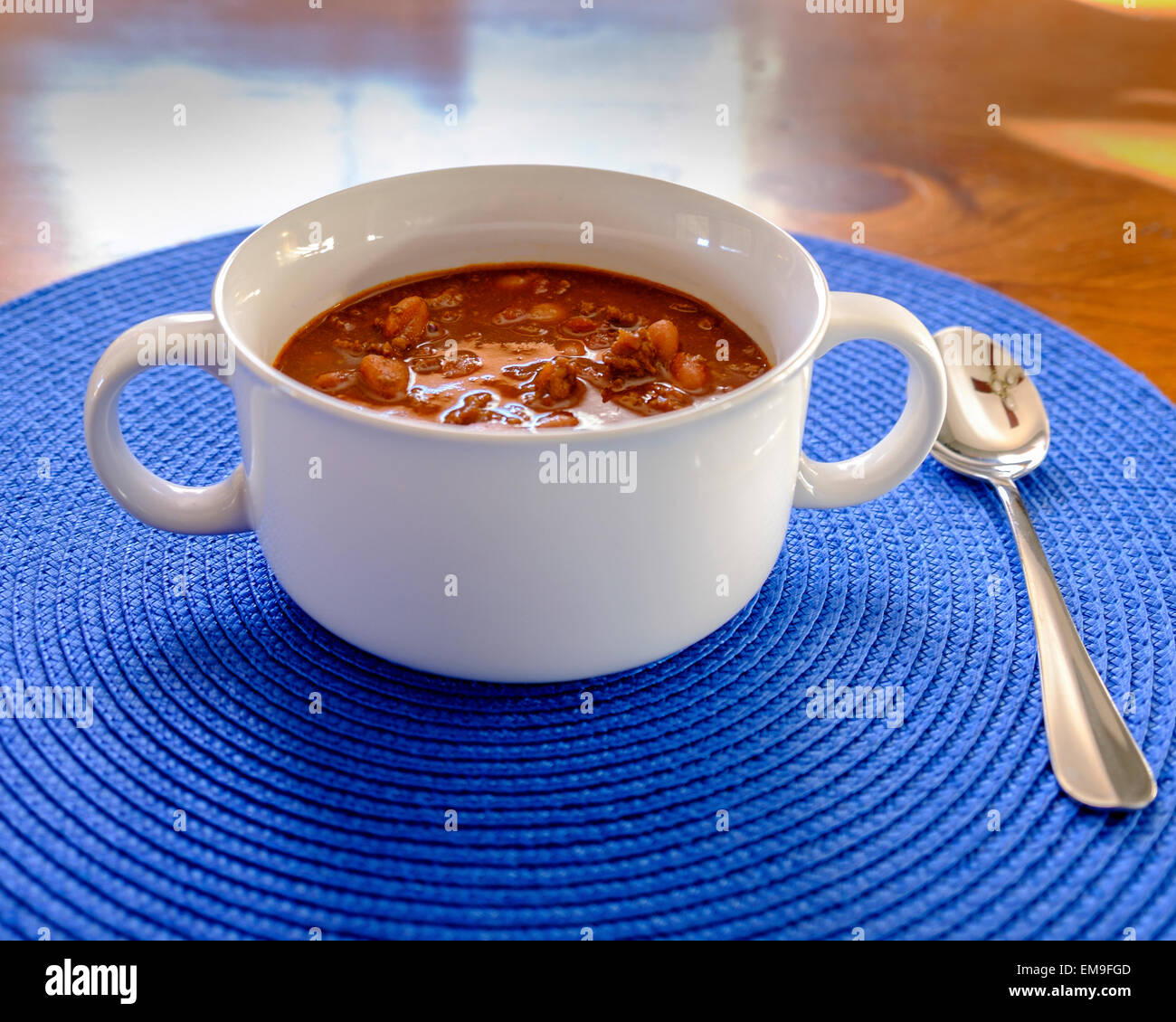 A bowl of homemade beef chili with beans in a white bowl on a blue placemat. USA Stock Photo