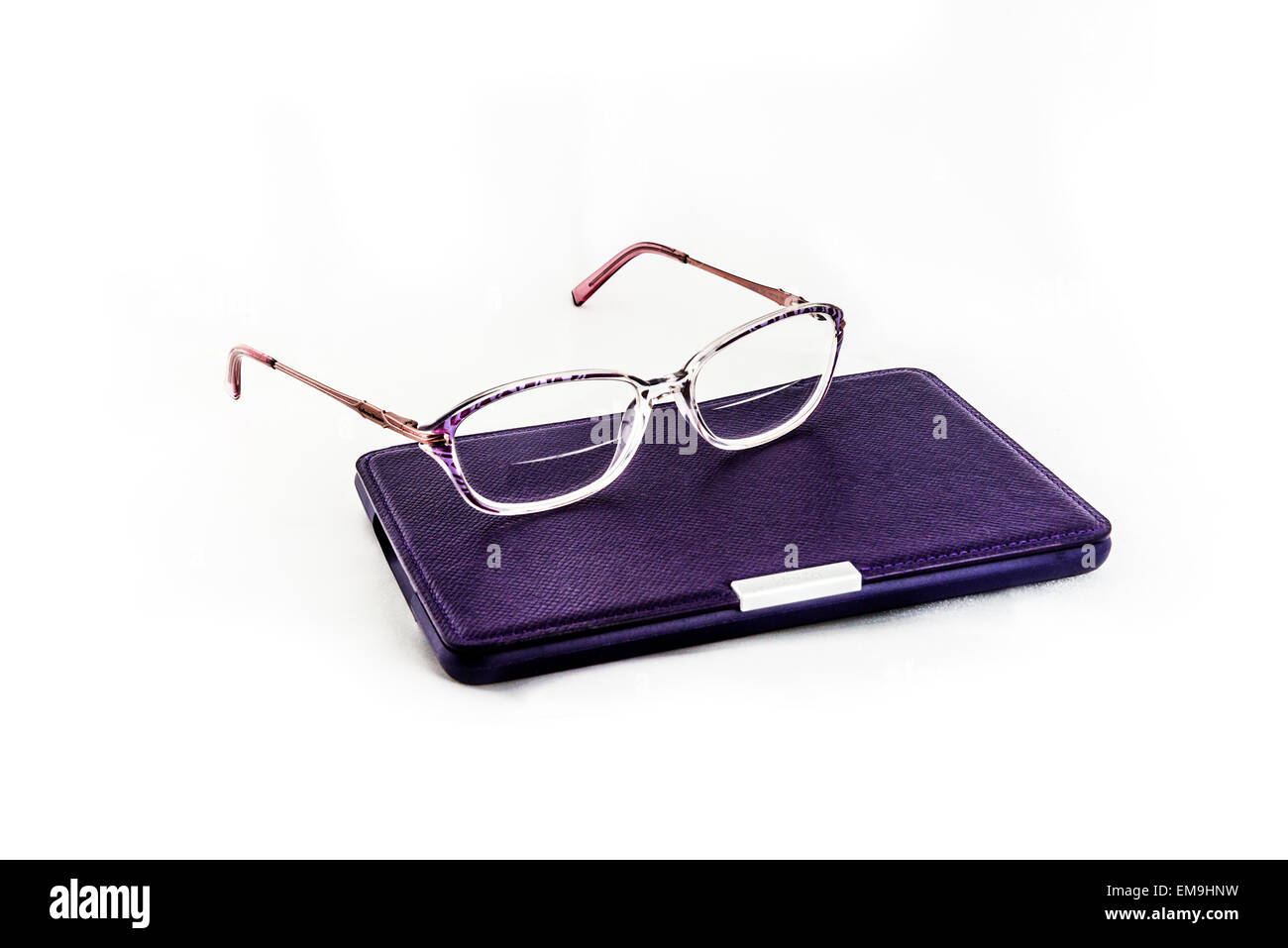A pair of women's bifocal eyeglasses lying atop a Kindle Paperwhite reader in a purple case. Isolated on white. USA. Cutout. Stock Photo