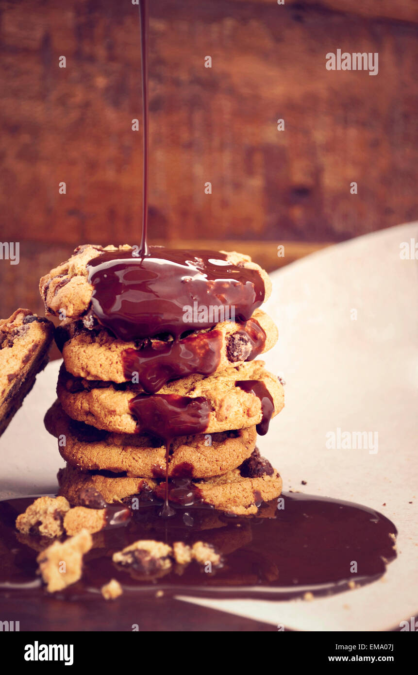 Chocolate sauce pouring over a stack of chocolate chip cookies on white curling baking paper
