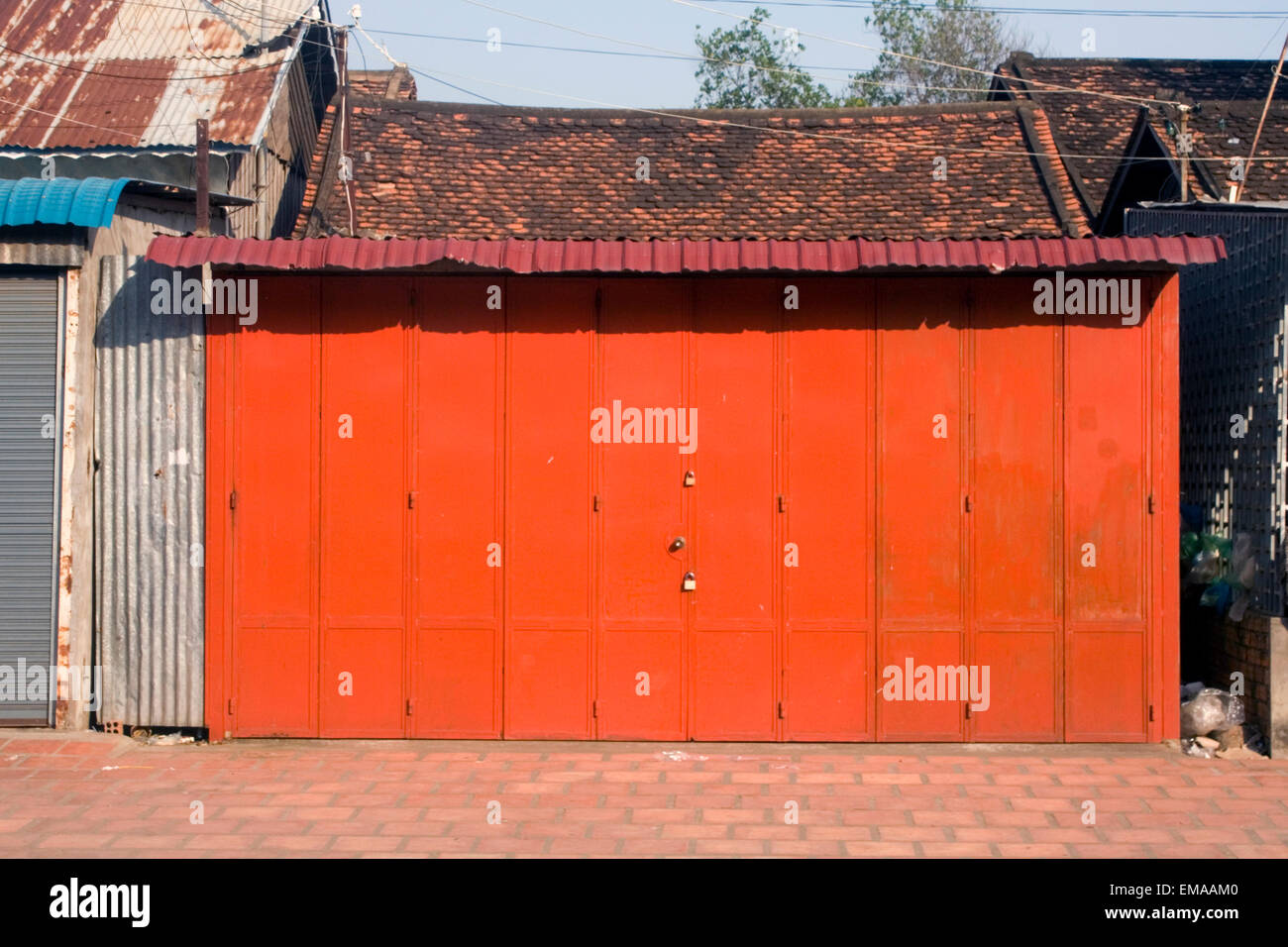 A bright red metal door stands padlocked on a city street in Kampong Cham, Cambodia. Stock Photo