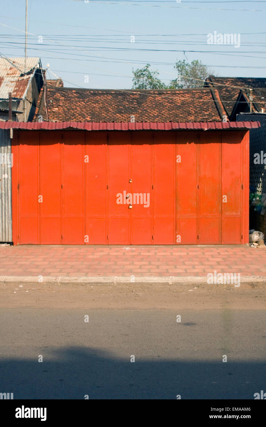 A bright red metal door stands padlocked on a city street in Kampong Cham, Cambodia. Stock Photo