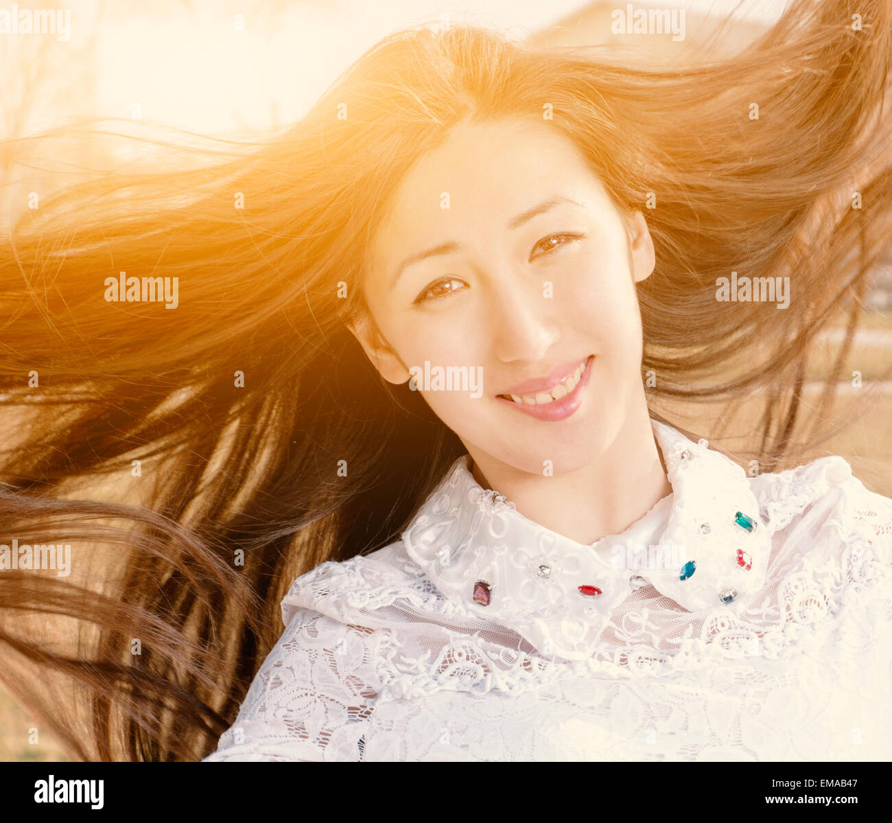 Beauty Romantic Girl Outdoors Closeup. Beautiful Asian Teenage Model Girl in Casual Dress with Jevels in Sun Light. Blowing Long Stock Photo