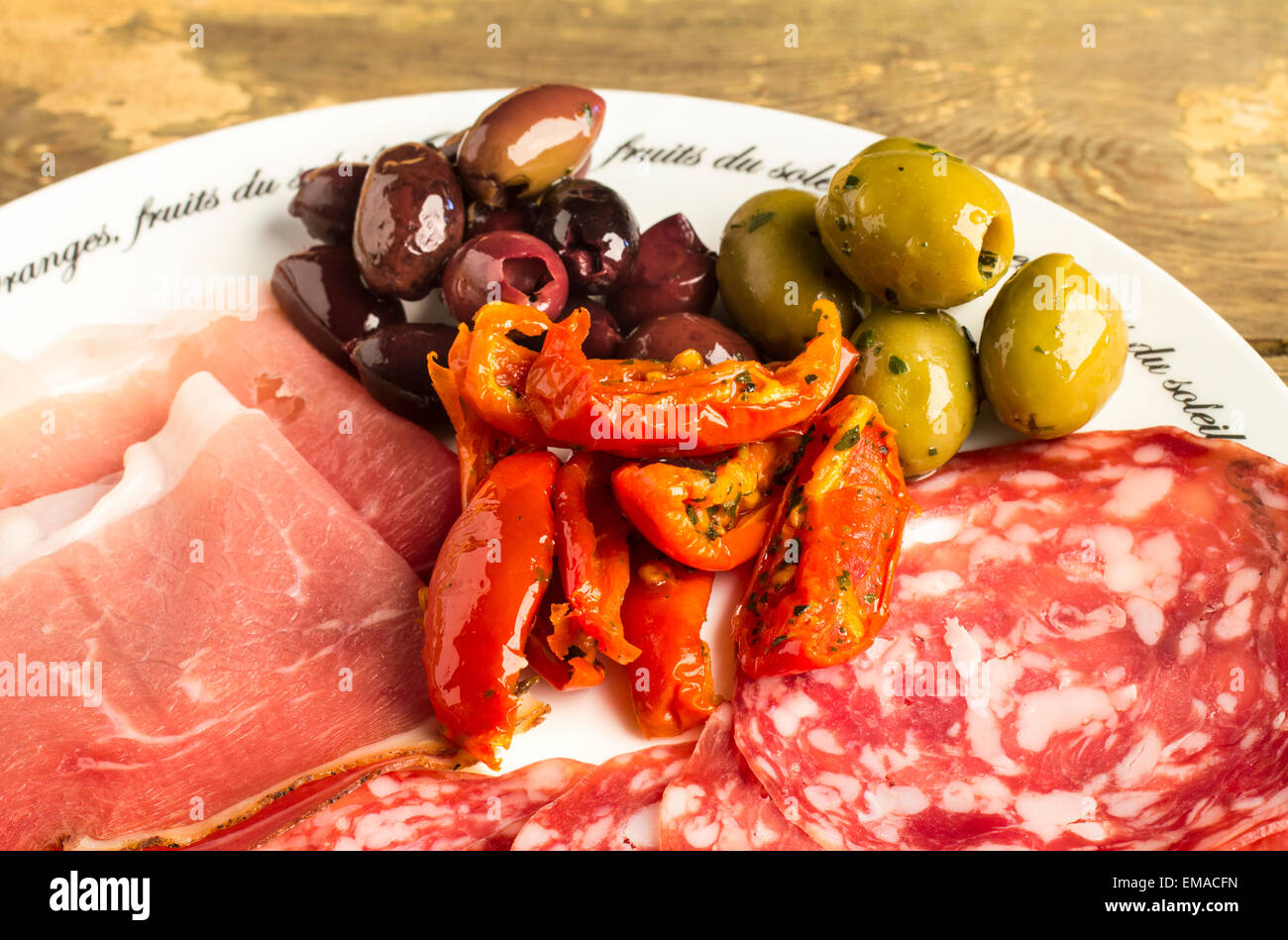 A plate of  antipasti: Greek Halkidiki olives, Kalamata Olives, semi dried tomatoes, Italian Prosciutto and salami Stock Photo