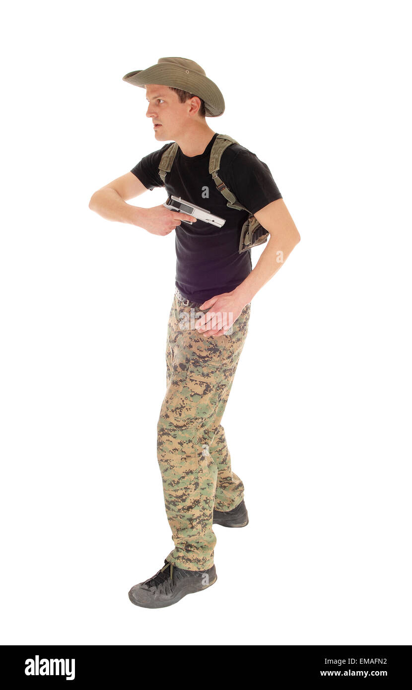A soldier in camouflage pants, hat and black t-shirt pulling his hand gun out of the holster, isolated on white background. Stock Photo