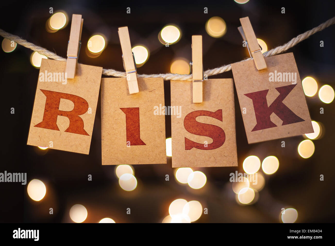 The word RISK printed on clothespin clipped cards in front of defocused glowing lights. Stock Photo