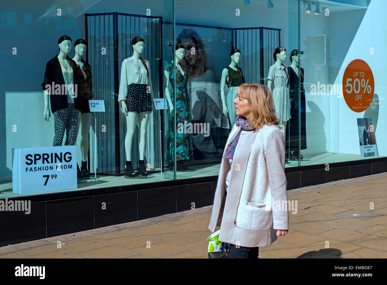 A lone middle-aged woman walks by a window display of Spring fashion on Princes Street, Edinburgh, Scotland. Stock Photo