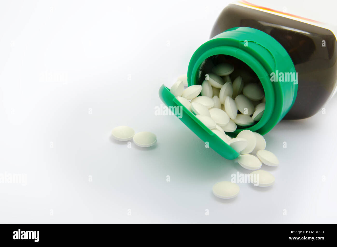 Small white pills spilling out of a green bottle Stock Photo