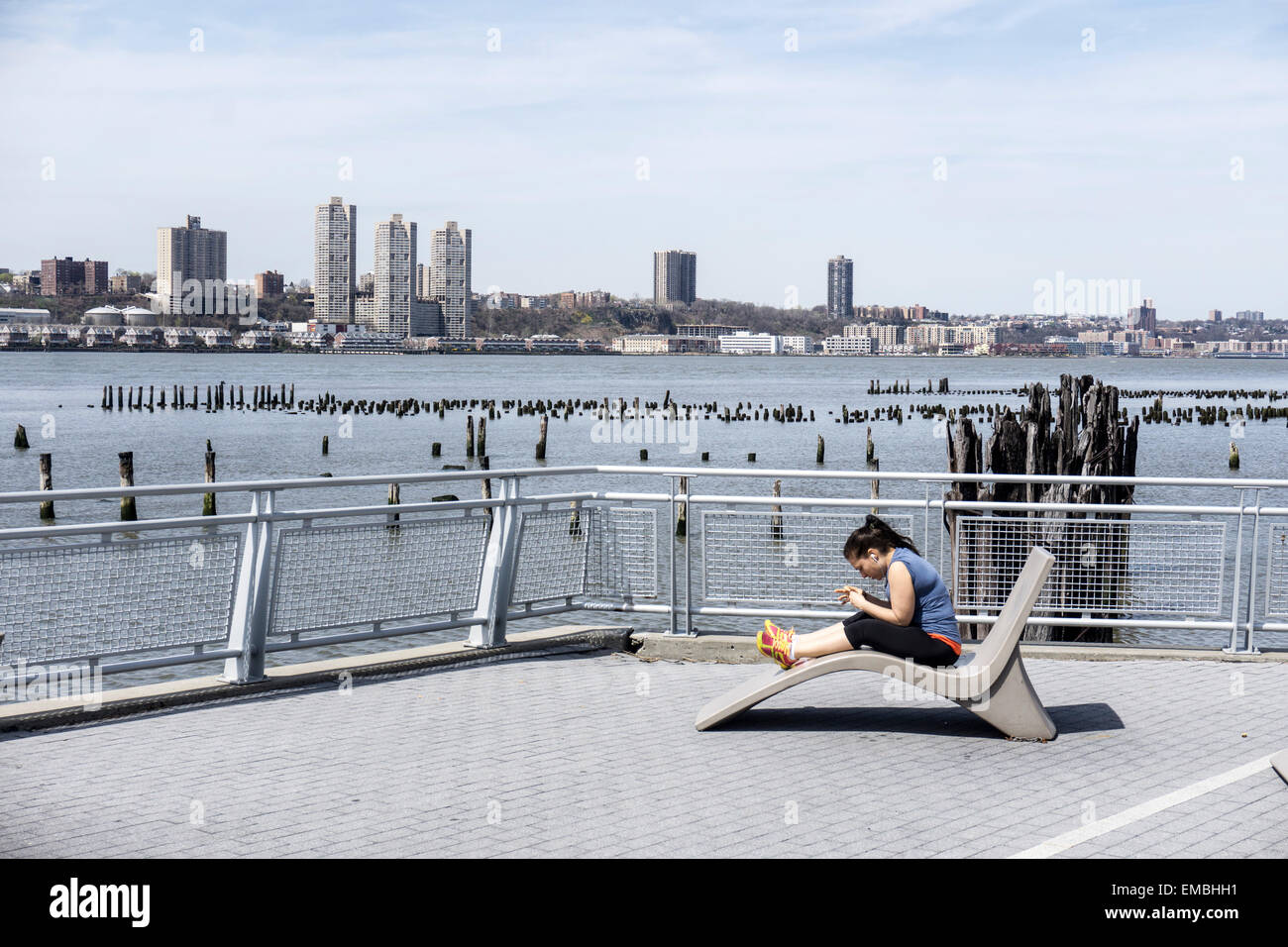 New York City, USA. Sunday April 19, 2015, USA; woman enjoys spring Sunday sitting on permanent outdoor chaise longue with panoramic view of Hudson River, picturesque old pier pilings & New Jersey Palisades Credit:  Dorothy Alexander/Alamy Live News Stock Photo