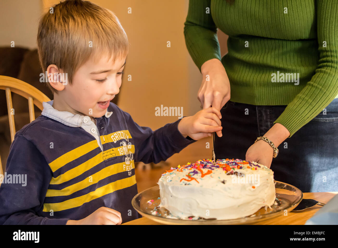 Seven year old boy helping his mother cut his birthday cake in Issaquah, Washington, USA Stock Photo