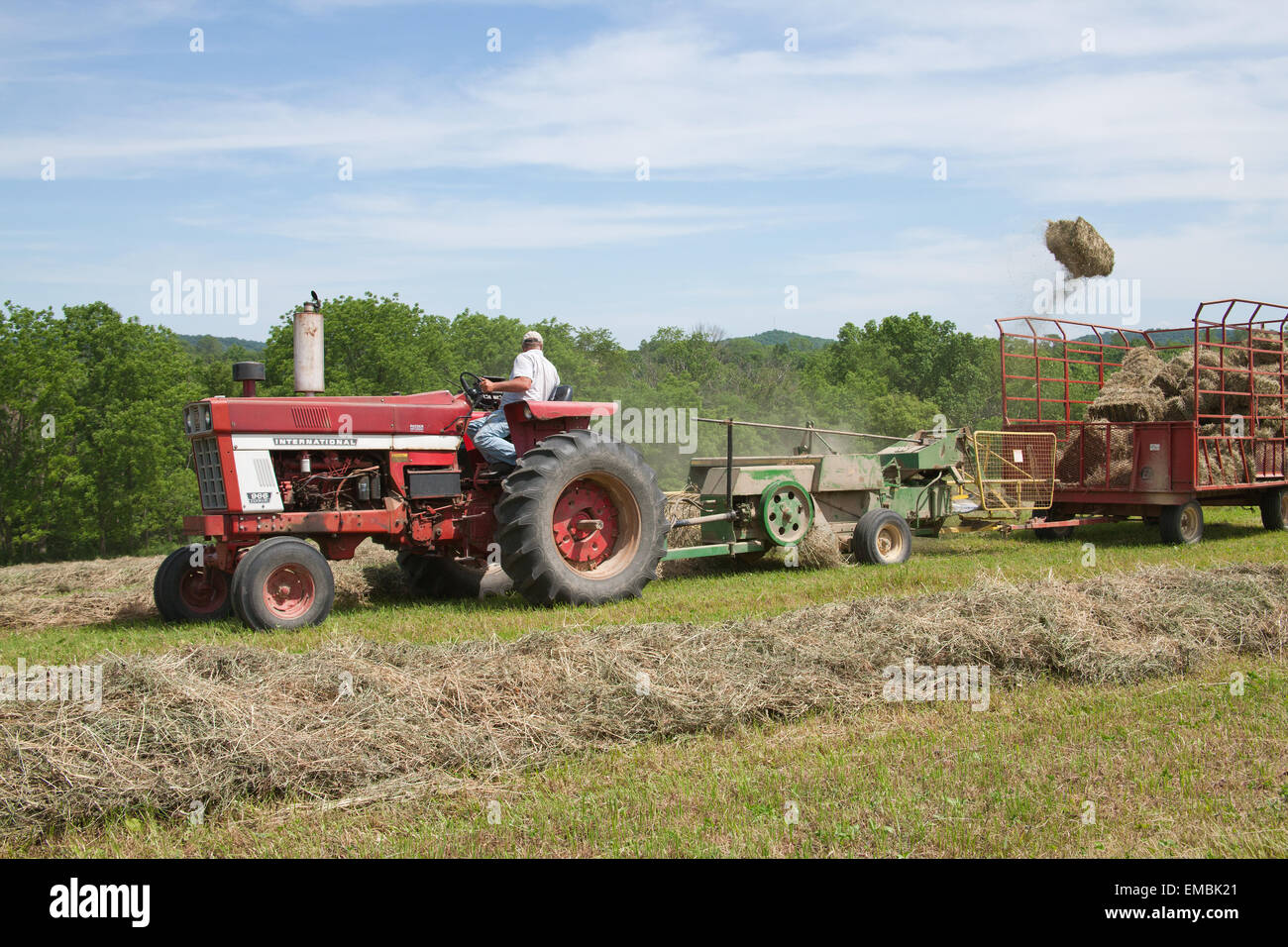 Man on International Harvester Farmall tractor, baling hay in a field with a bale flying in the air, near Galena, Illinois, USA Stock Photo
