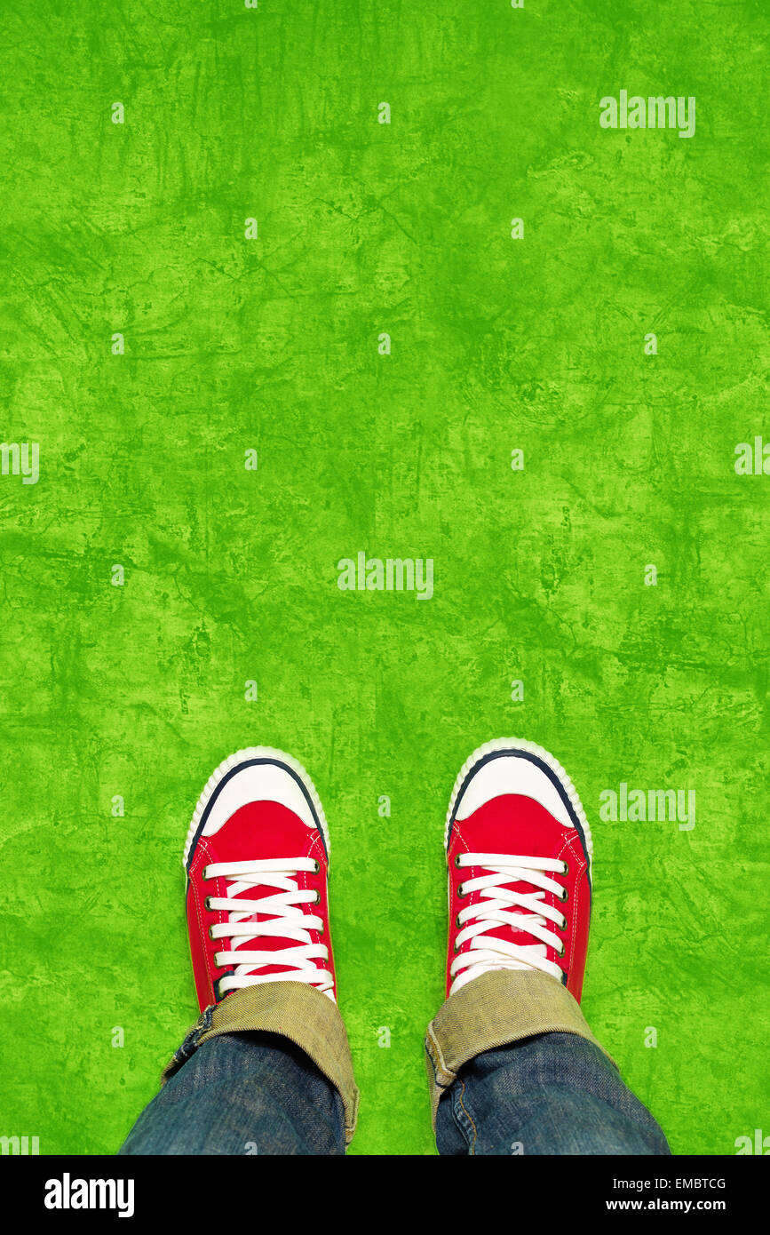 Feet From Above Concept, Teenage Person in Red Sneakers Standing on Green Background, Blank Copy Space in Front, Top View Stock Photo