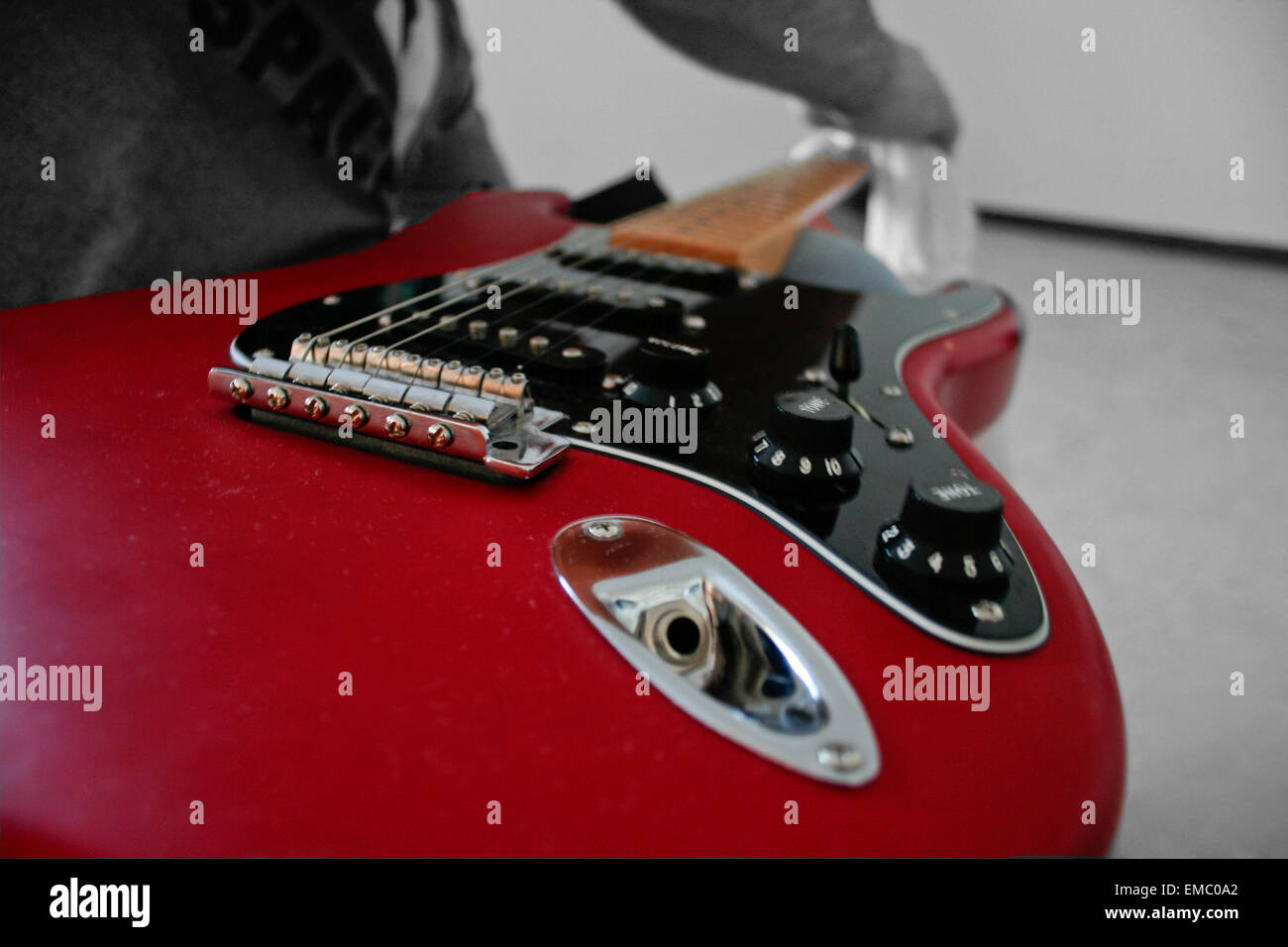 Unidentified man cleans his electric guitar neck with a white rag over the knees Stock Photo