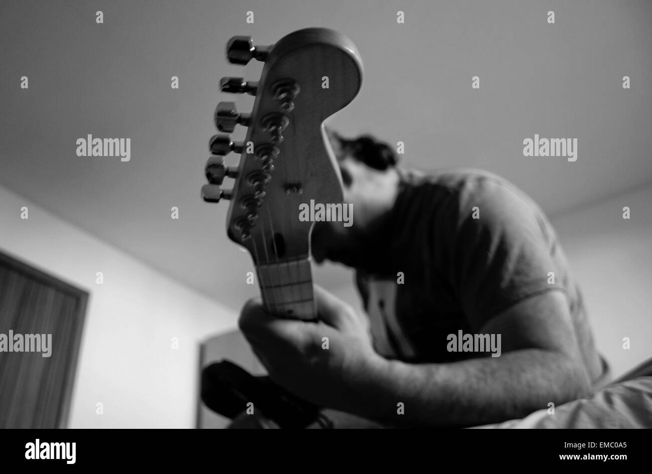 Unidentified man cleans his electric guitar neck with a white rag over the knees. Black and white shot Stock Photo