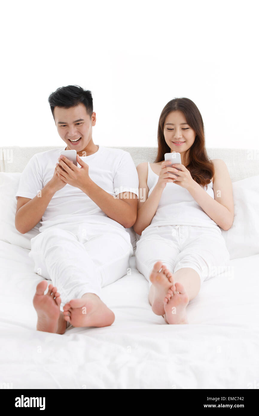 The young couple playing mobile phone on the bed in the bedroom Stock Photo