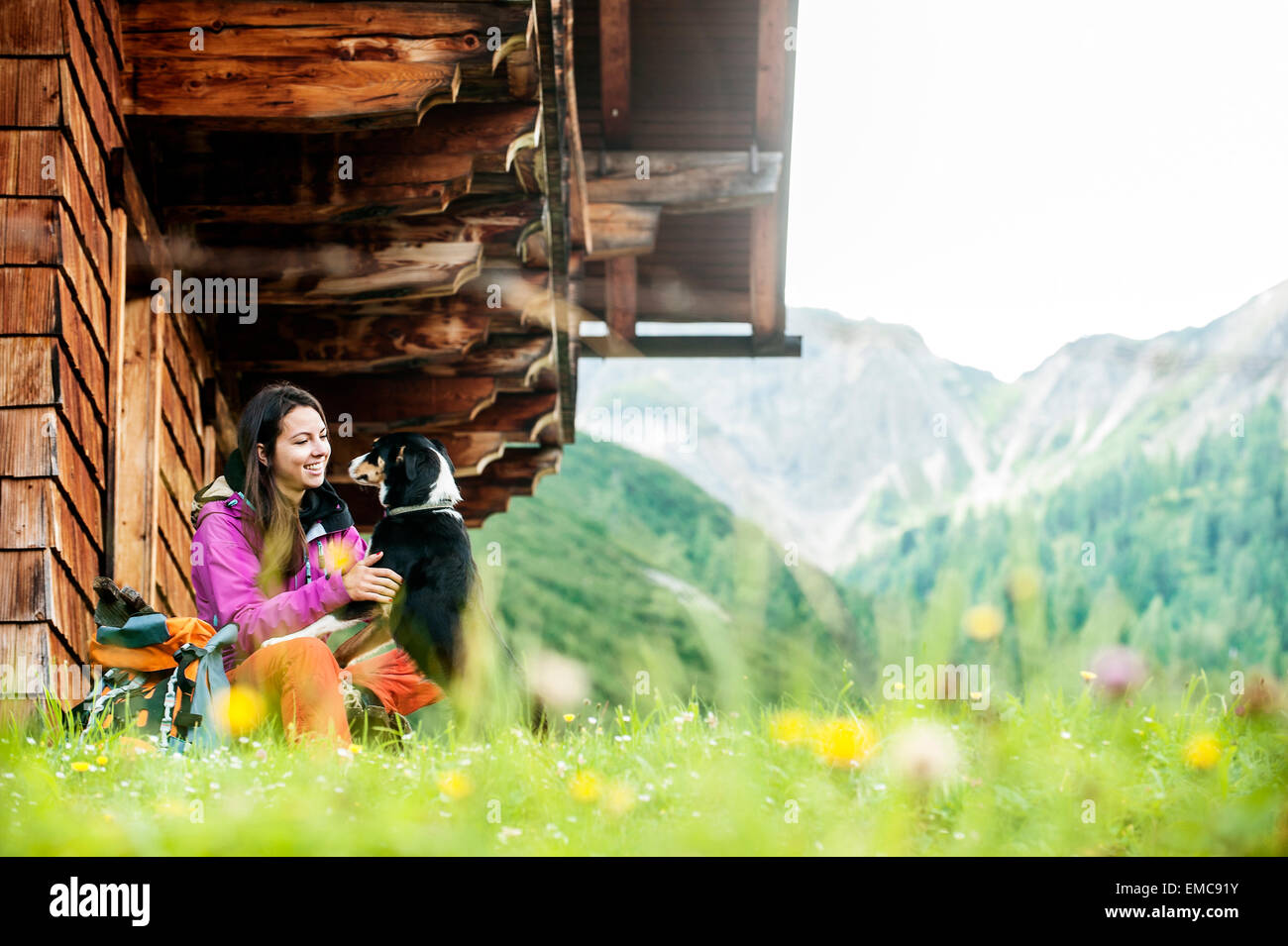 Austria, Altenmarkt-Zauchensee, young woman and dog in front of an Alpin cabin Stock Photo
