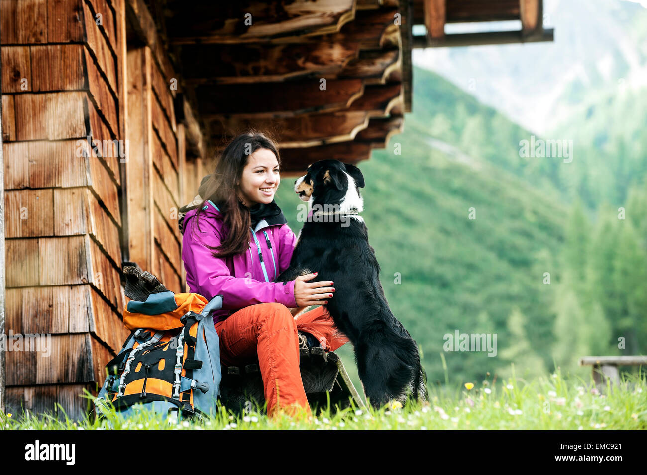 Austria, Altenmarkt-Zauchensee, young woman and dog in front of an Alpin cabin Stock Photo