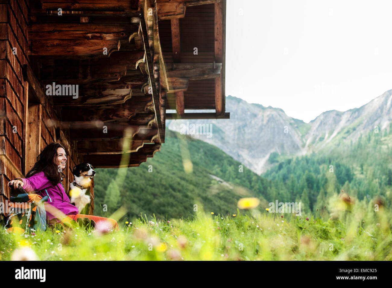 Austria, Altenmarkt-Zauchensee, young woman and dog in front of an Alpin cabin Stock Photo
