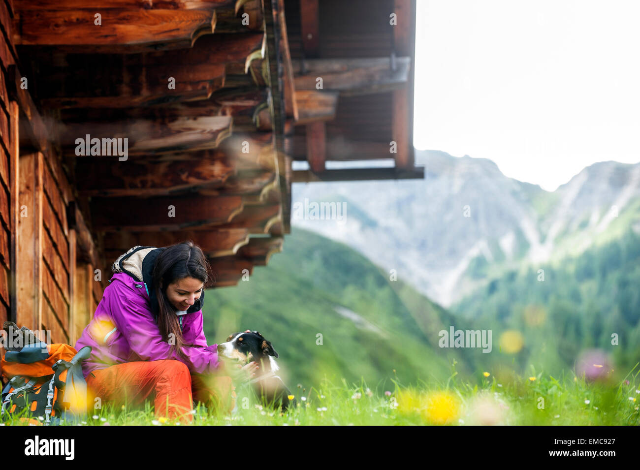Austria, Altenmarkt-Zauchensee, young woman and dog in front of an Alpin cabin Stock Photo