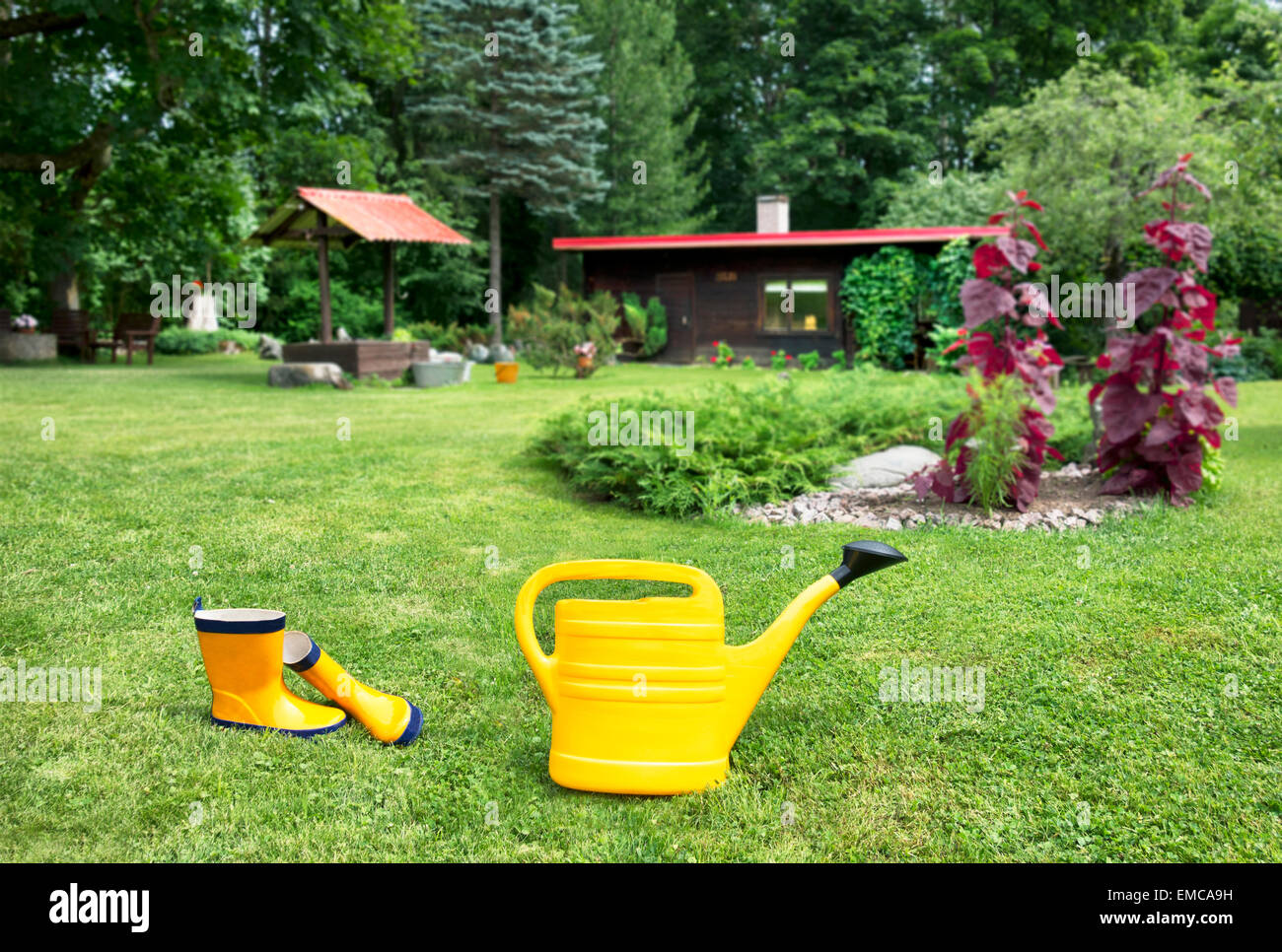 Estonia, yellow watering can and Wellington boots on the meadow in the ...