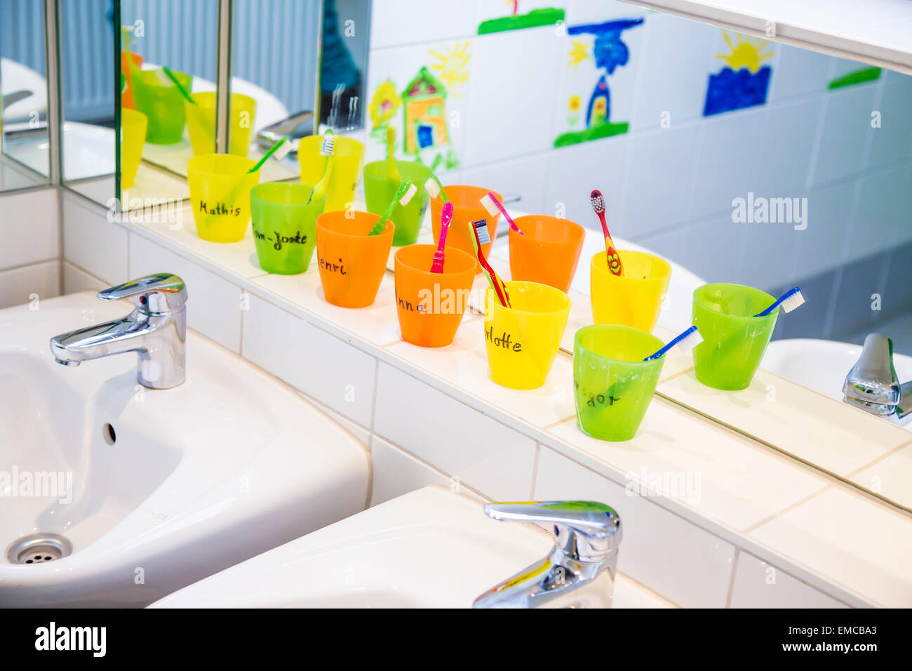 Plastic cups with toothbrushes with manes of kids in nursery Stock Photo