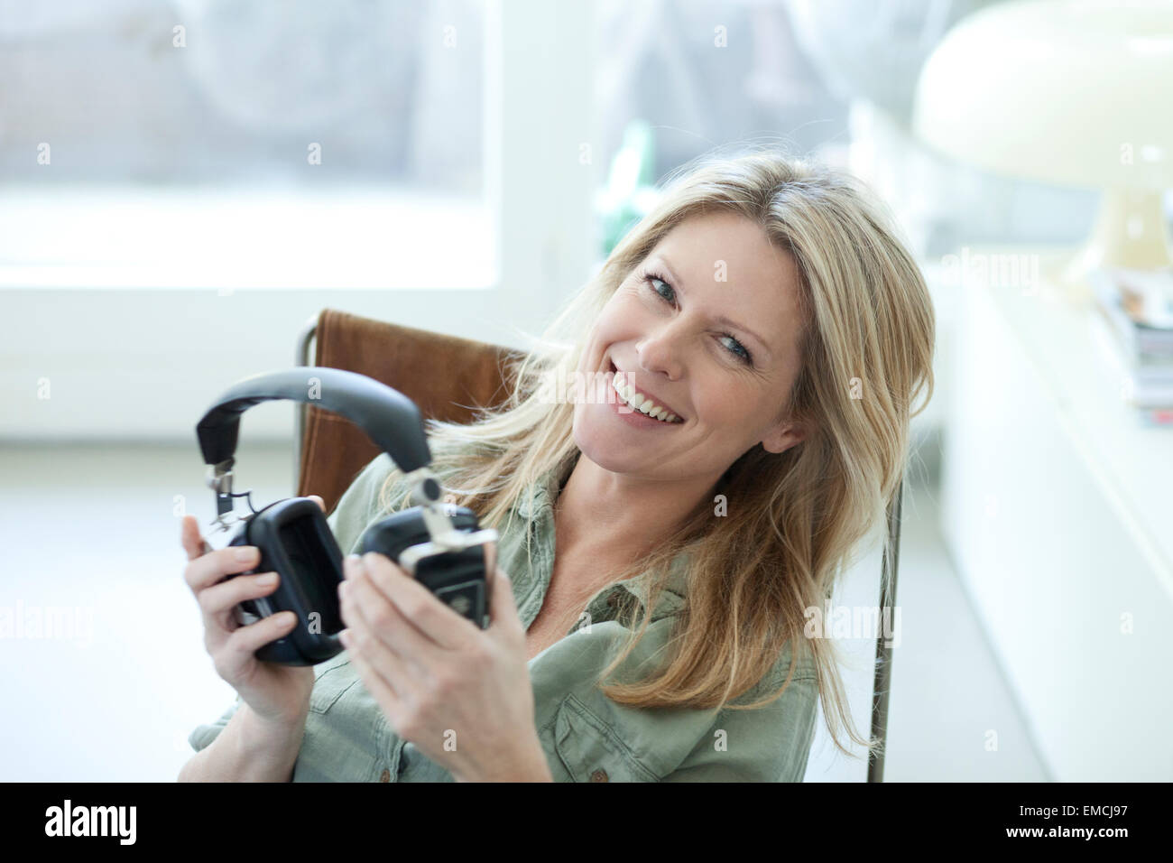 Portrait of smiling blond woman holding headphones Stock Photo - Alamy