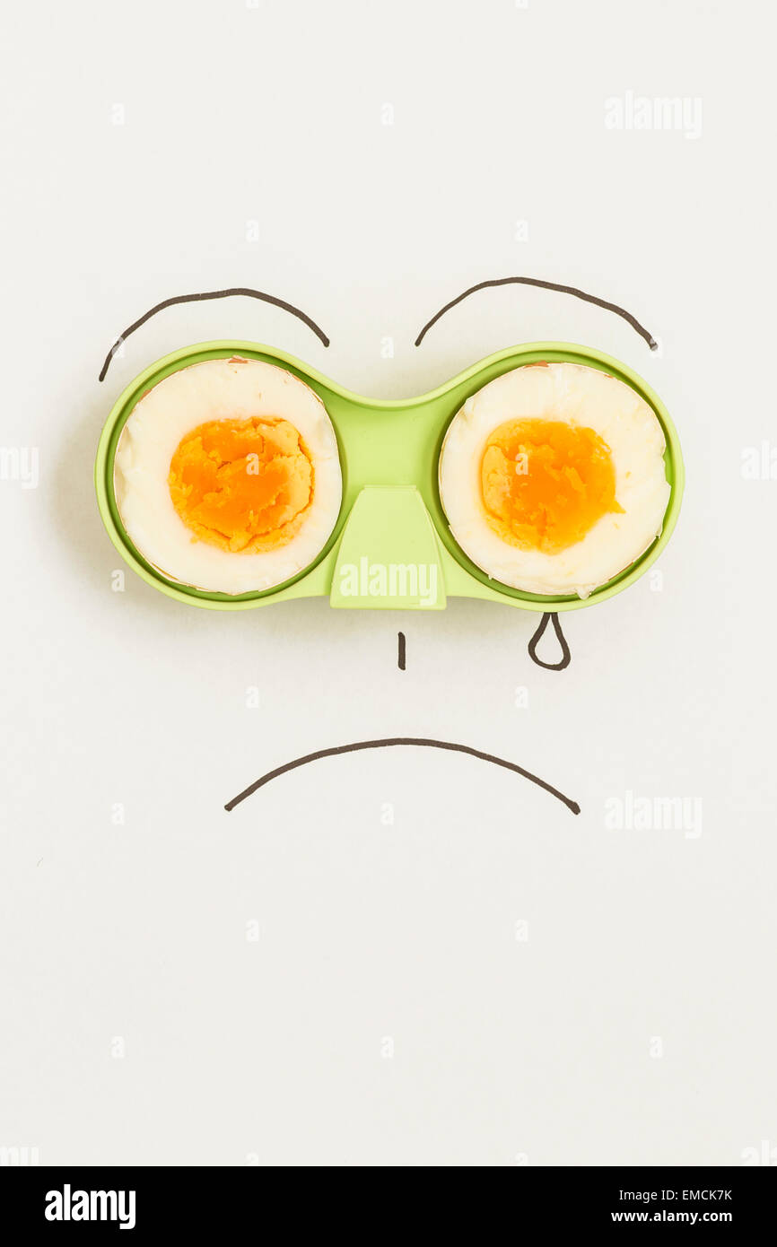 Two halves of an egg in green holder with sad face drawn around it Stock Photo