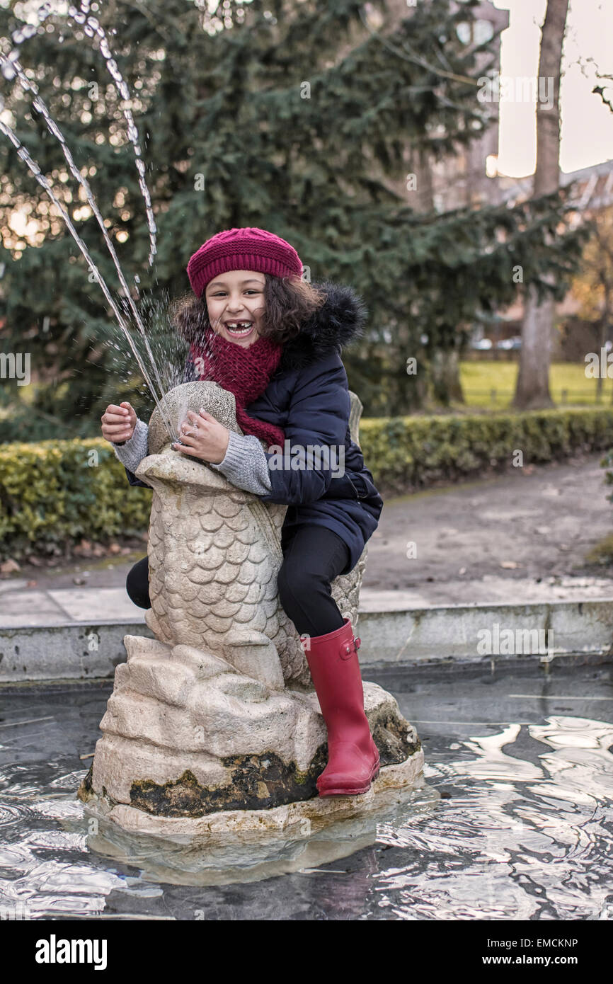 Portrait of smiling little girl sitting on sculpture of a fountain Stock Photo