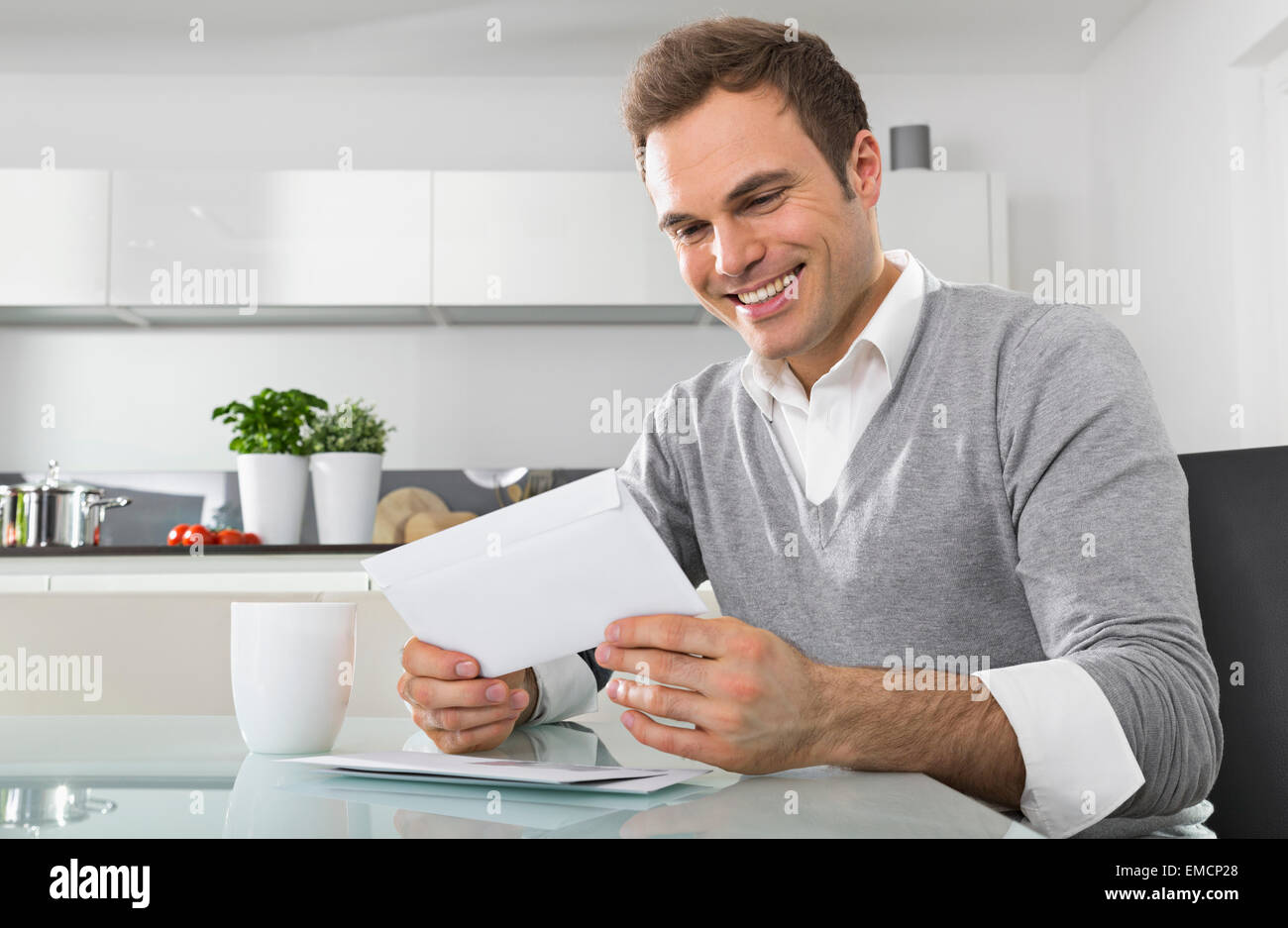 Smiling man sitting in kitchen watching envelope Stock Photo - Alamy