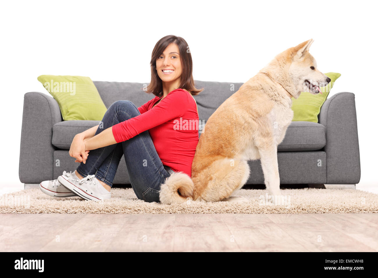 Young girl sitting on the floor in front of a gray sofa with her dog ...