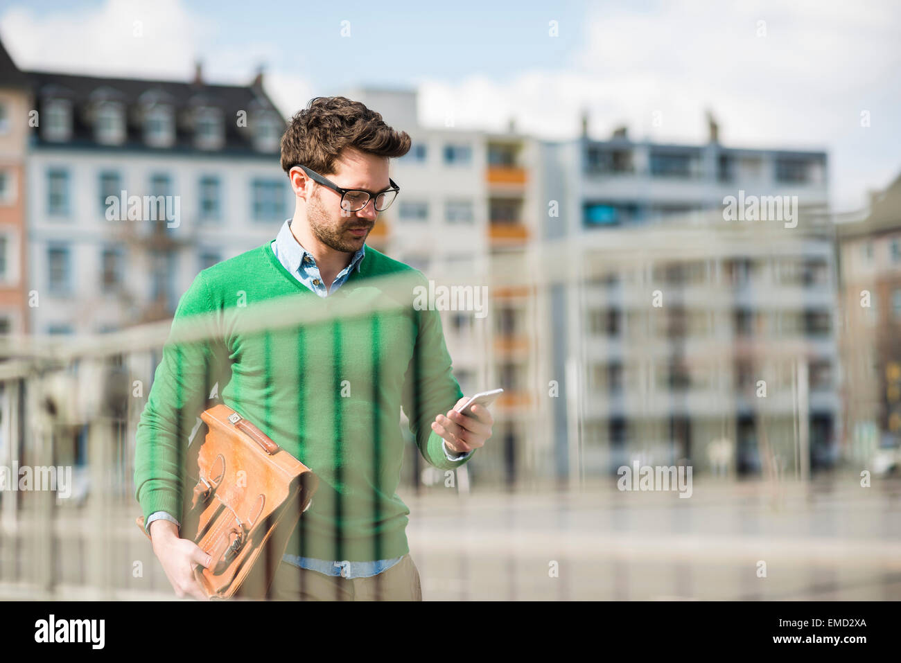 Man in green sweater carrying briefcase, reading text message Stock Photo
